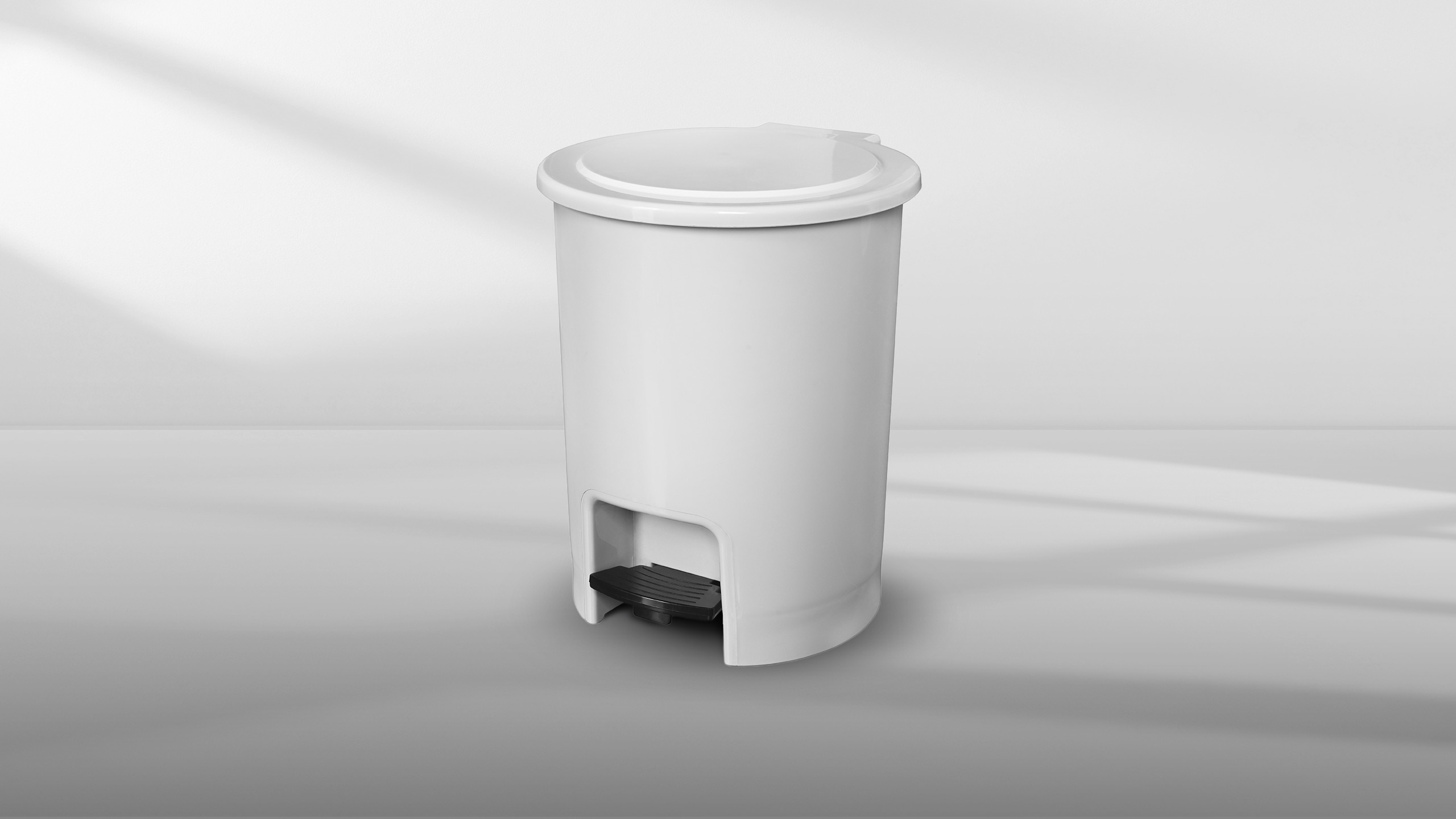 White plastic round pedal trash bin on a light surface with soft shadows.