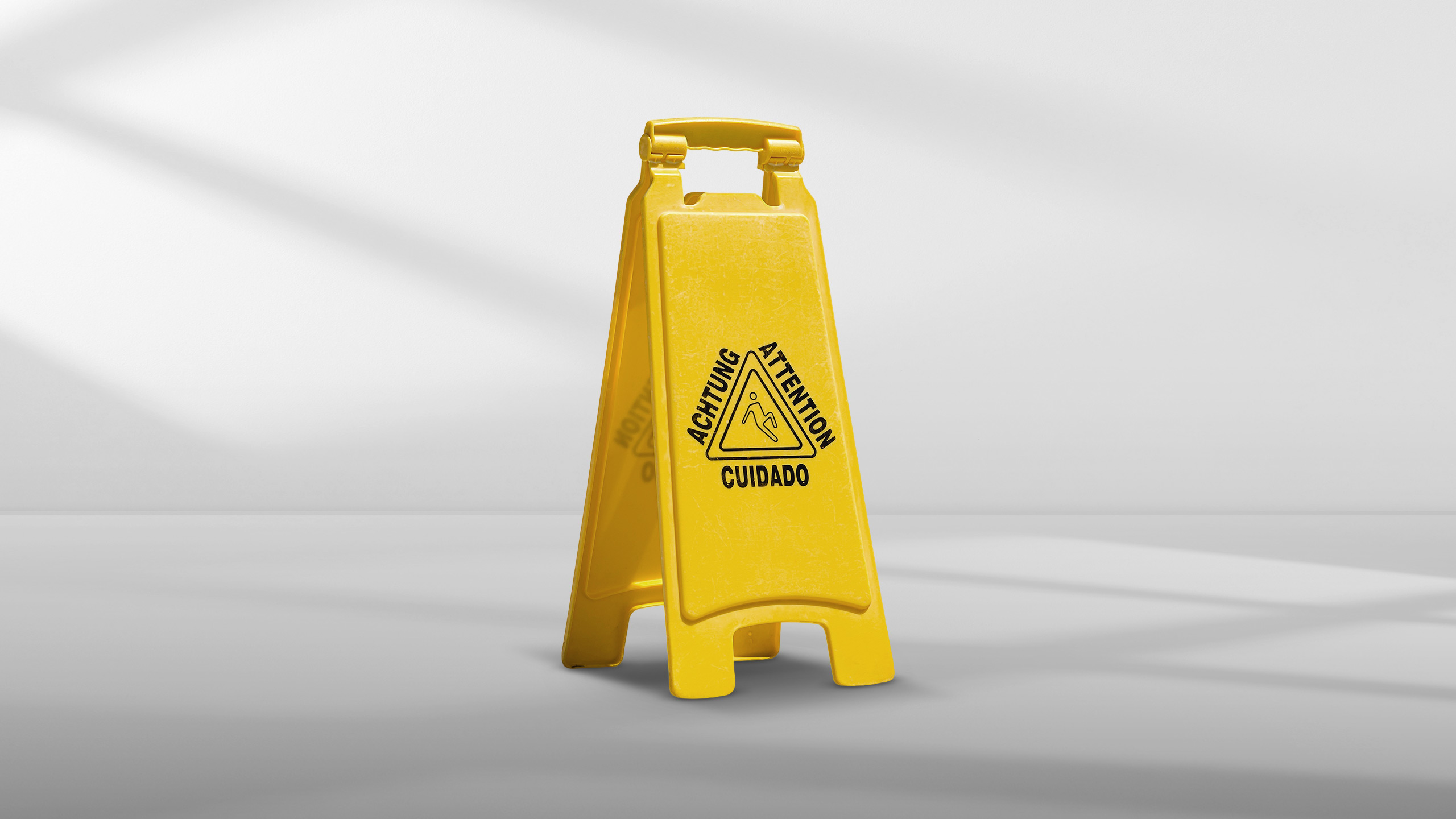 Yellow caution wet floor sign with warnings in German, English, and Spanish on a gray floor.