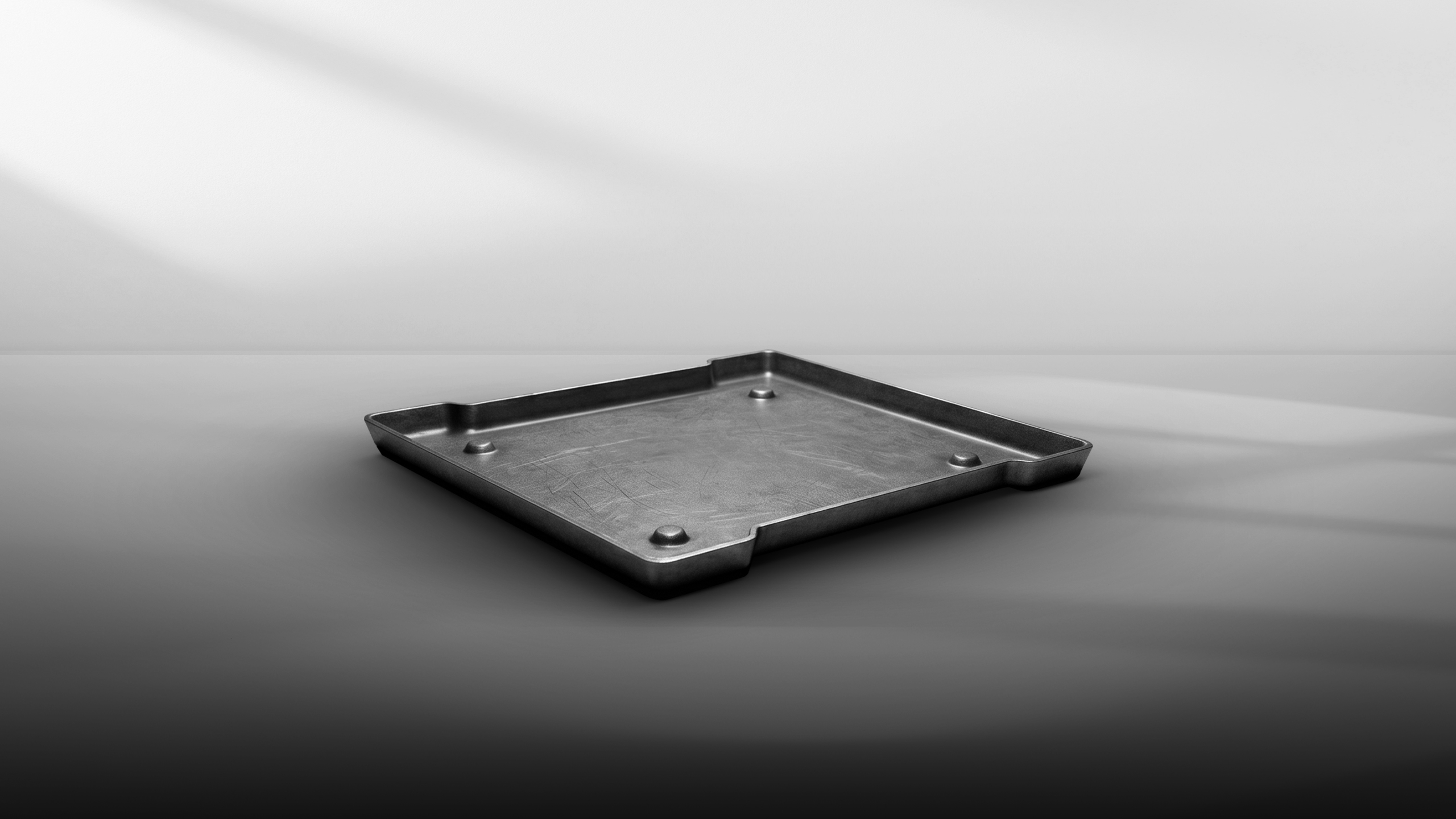 Empty square metal tray with raised edges and four small raised feet on smooth surface.