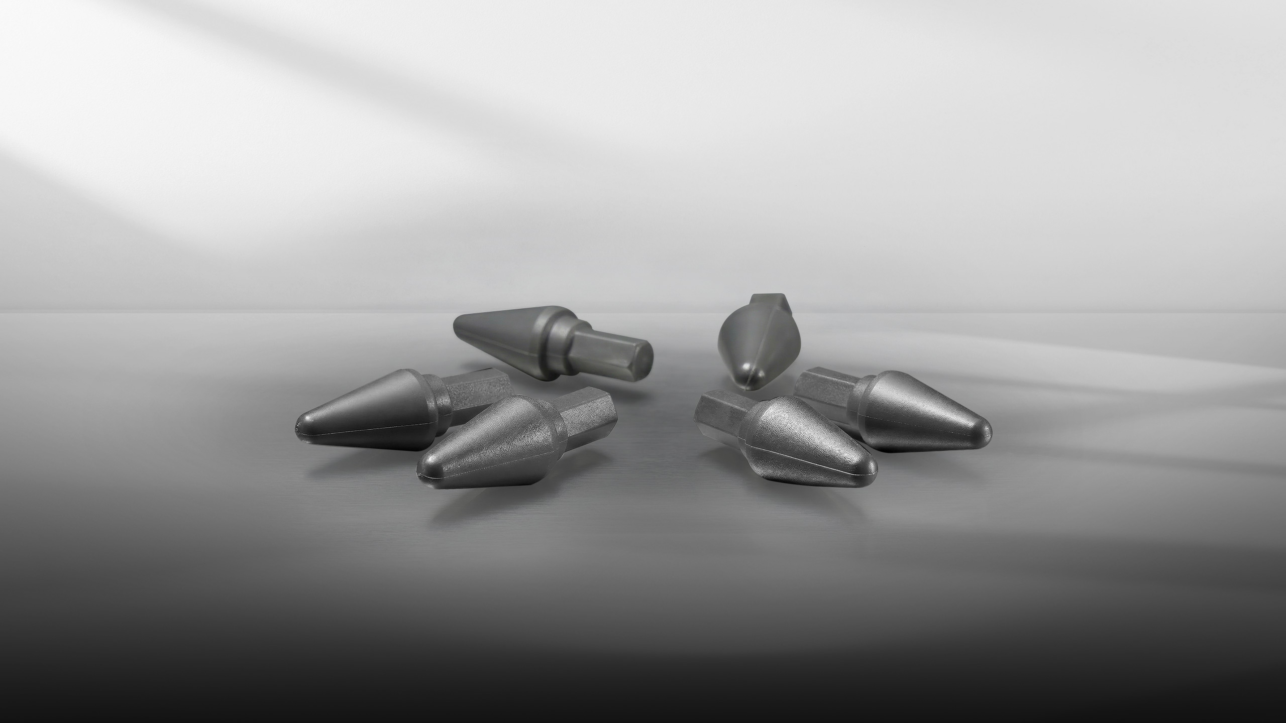 Six metallic screwdriver bits arranged on a reflective surface under soft lighting.