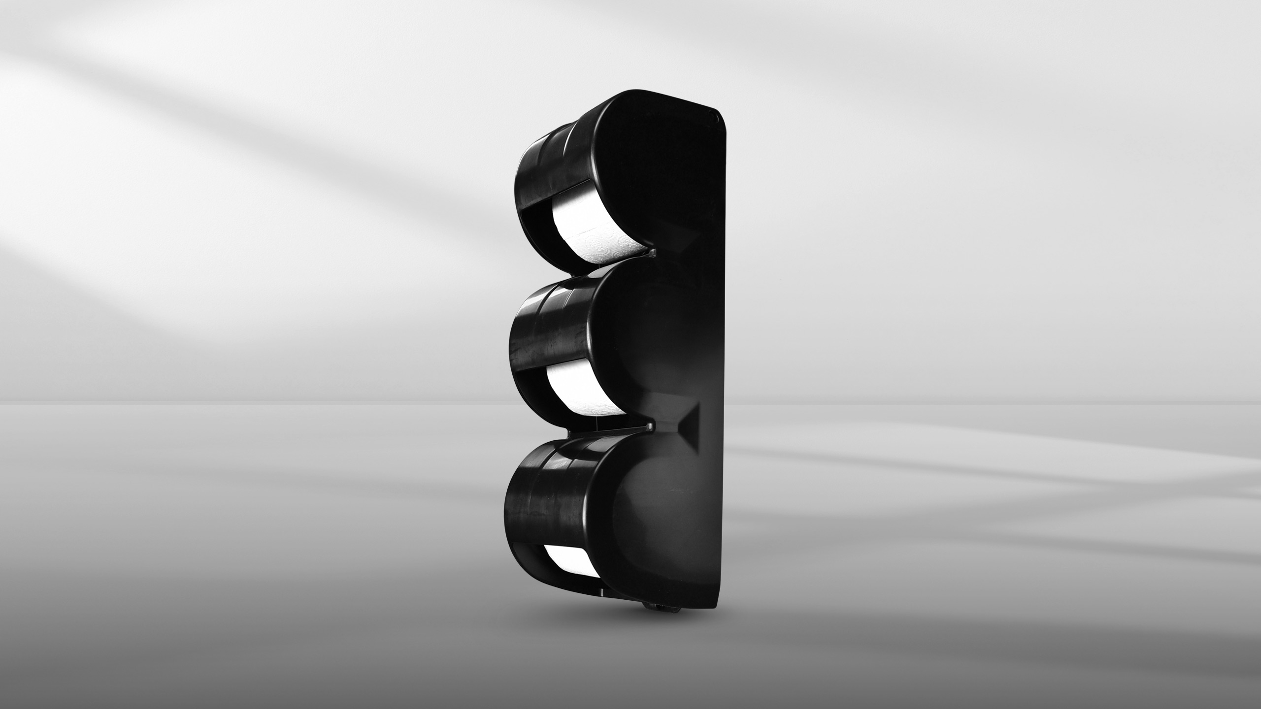 Black triple roll toilet paper dispenser stands against a gray background.