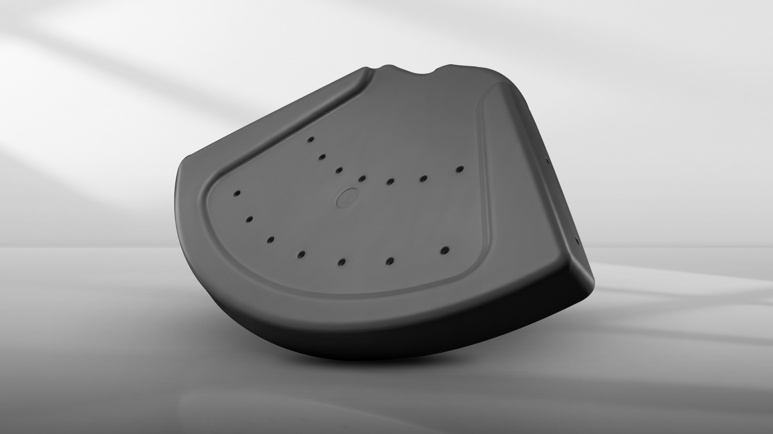 Black plastic curved object with multiple small holes on its surface against a gray background.