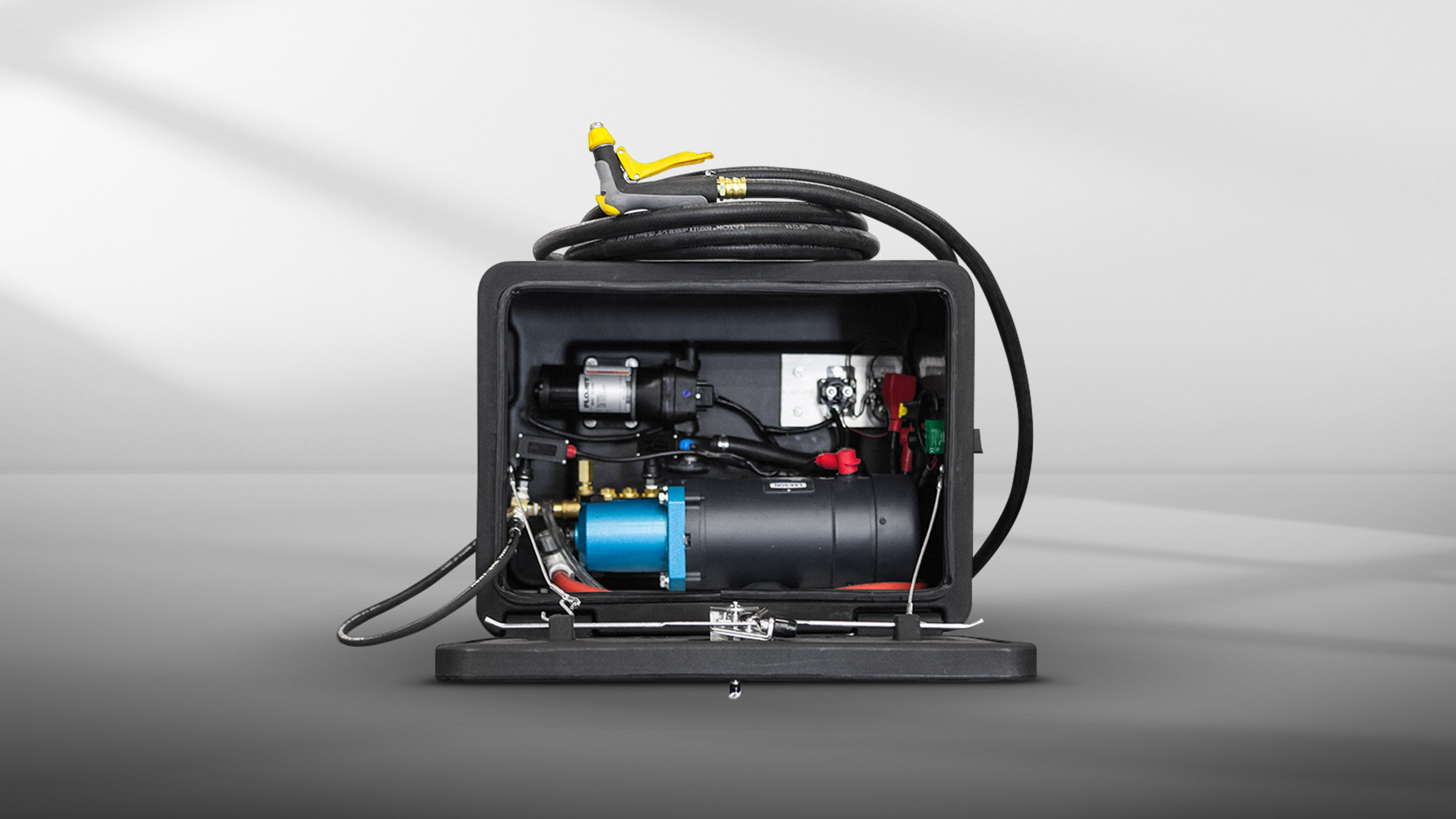 Open black case housing a motorized pump and coiled hoses with yellow spray nozzle.