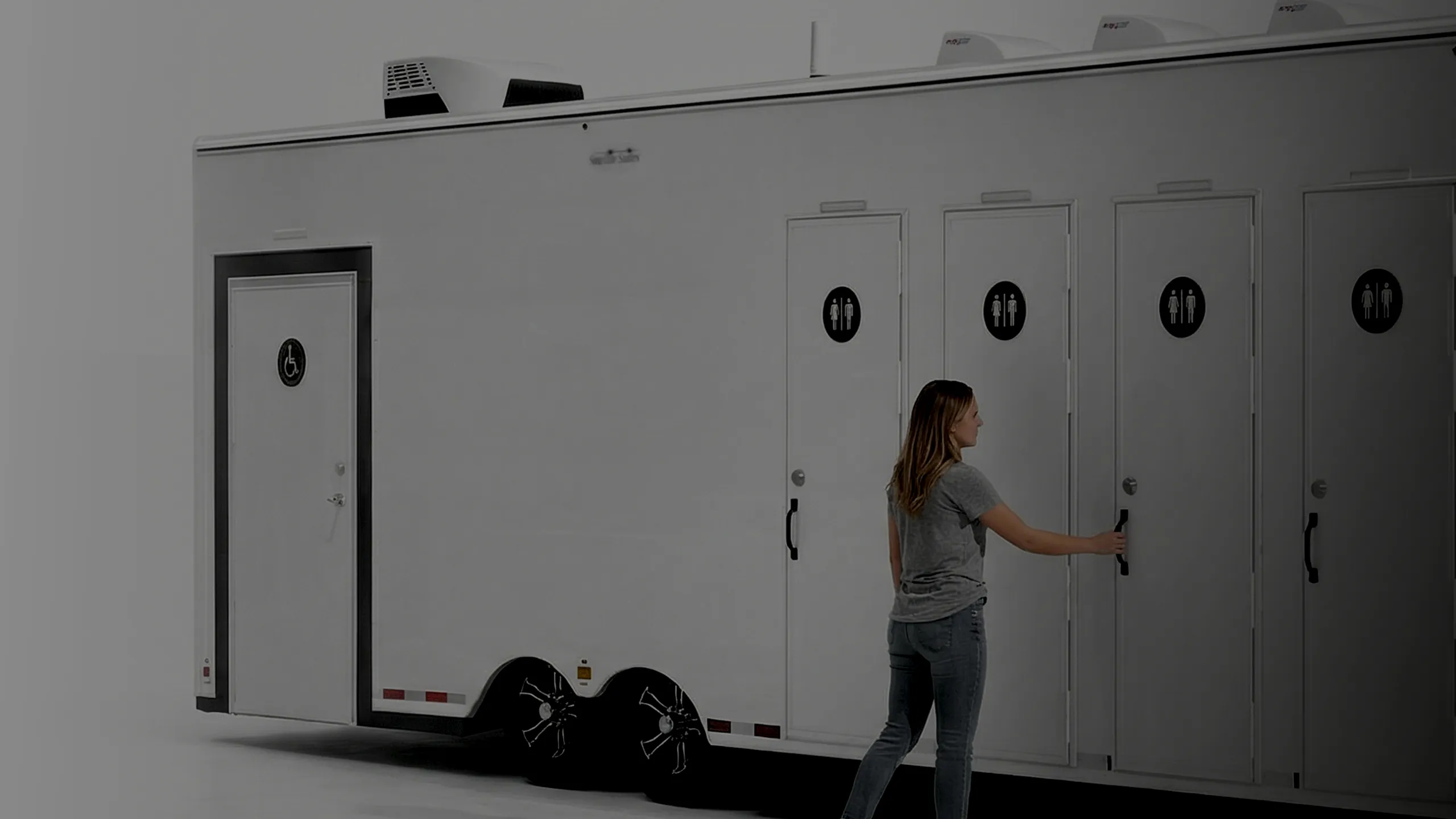 Woman opening a door on a trailer with several bathroom doors, including one with a wheelchair symbol.