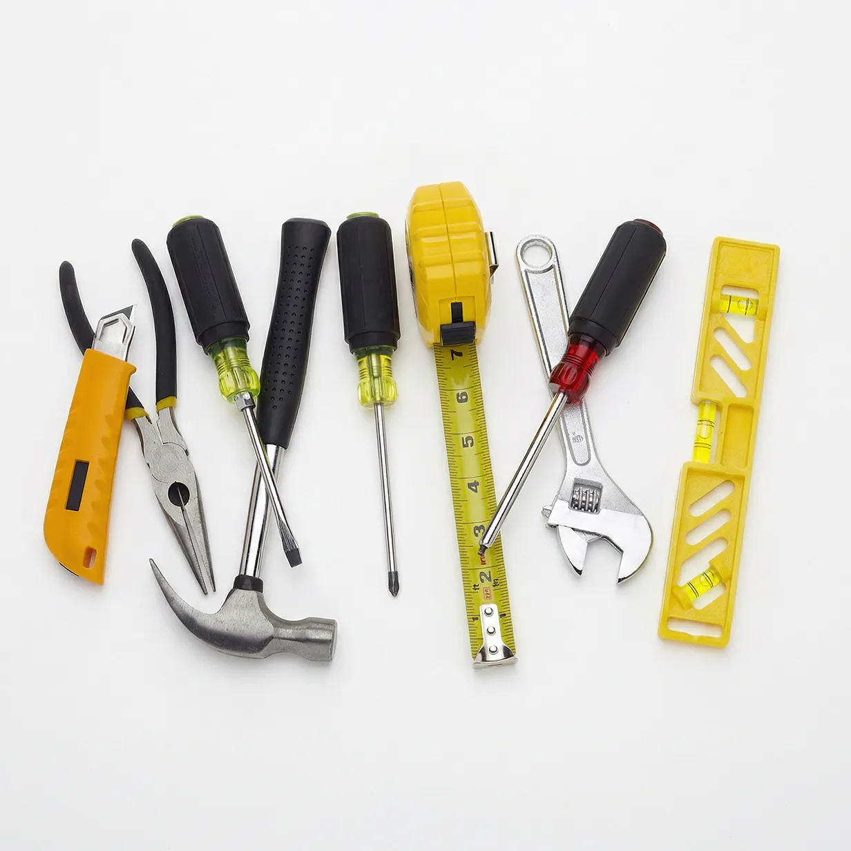 Set of hand tools on white surface including pliers, hammer, screwdrivers, tape measure, wrench, and level.