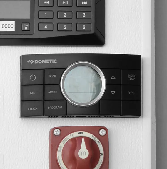 Dometic thermostat with buttons and circular display, mounted on a white wall above a red switch knob.