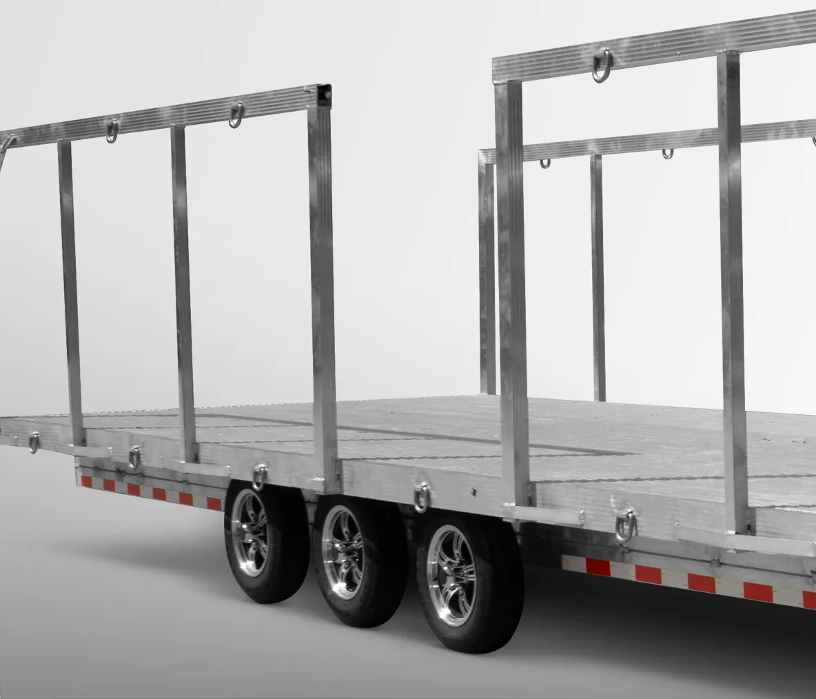 Close-up of a flatbed trailer with metal side rails and three wheels, shown on a plain background.