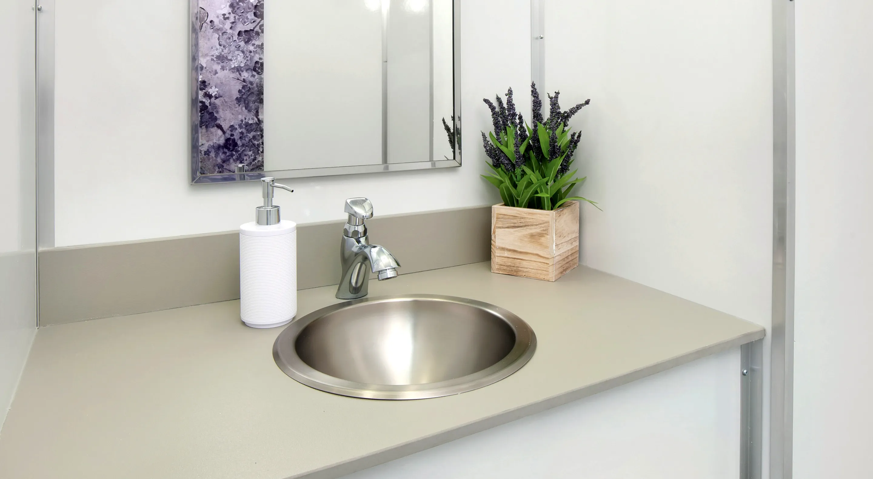 Modern bathroom sink with chrome faucet, white soap dispenser, and wooden planter with purple flowers.