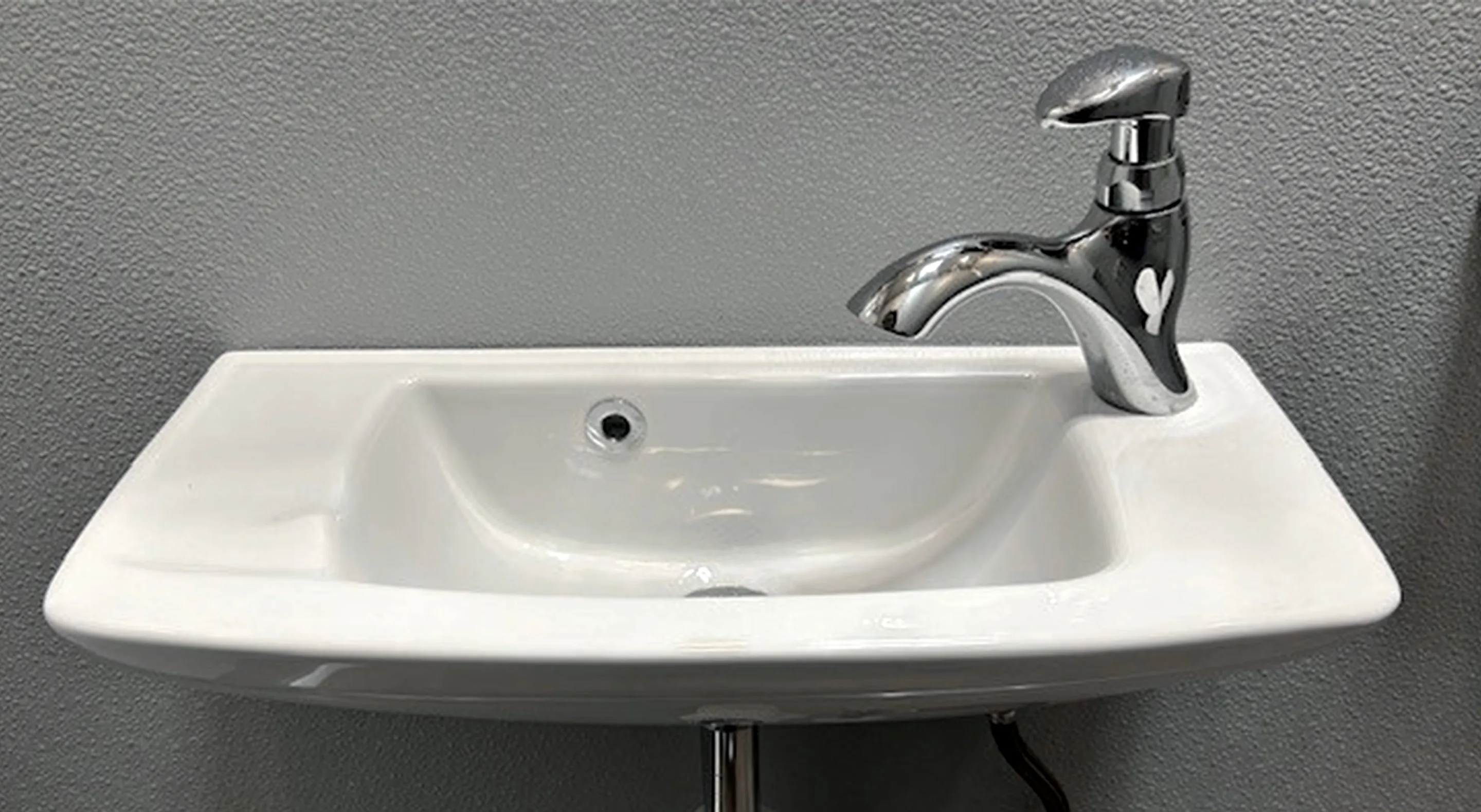 Wall-mounted white ceramic sink with a curved silver faucet and a gray textured wall background.