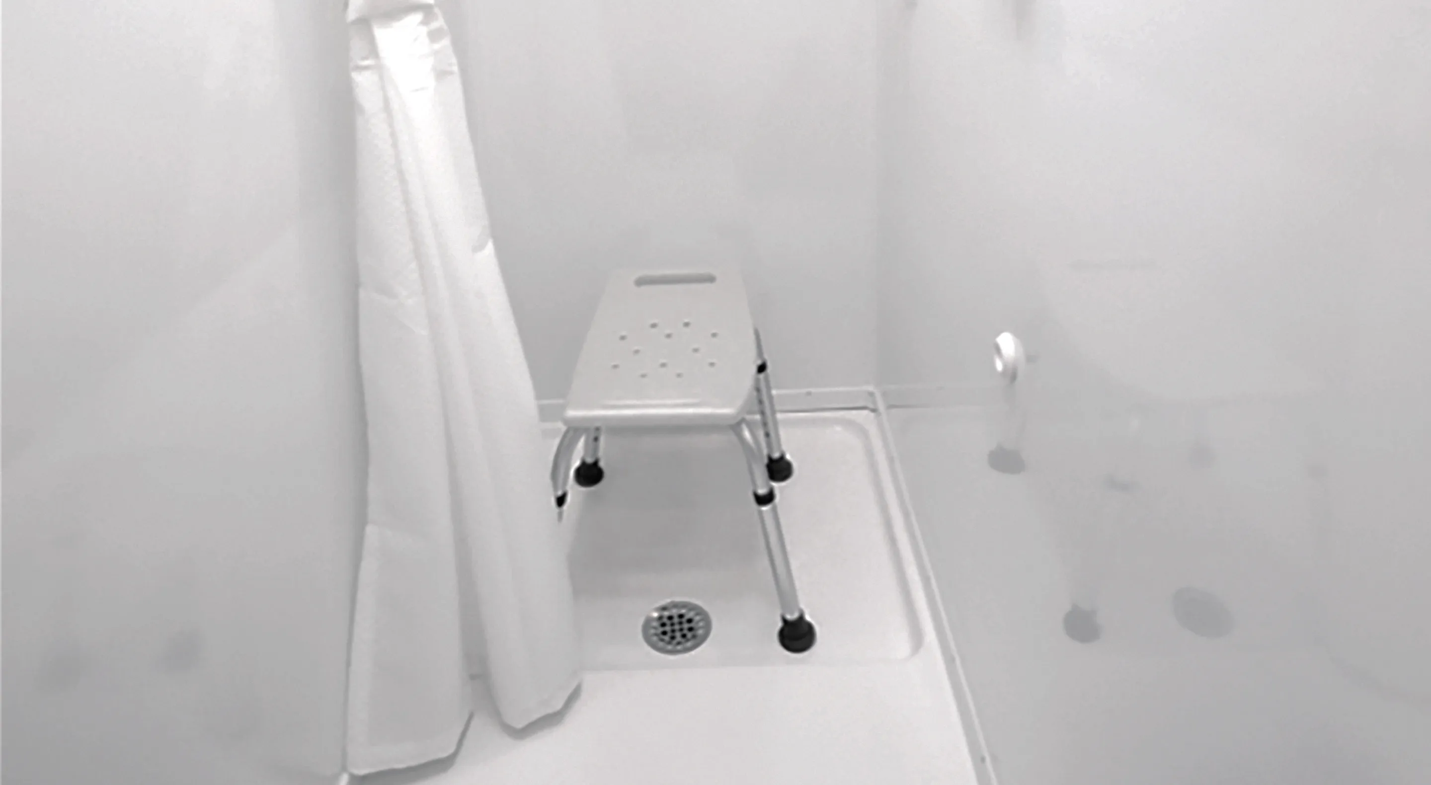 Small white shower stall with a shower chair and a white shower curtain partially drawn.